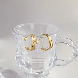 Gold triple-layered C-shaped hoop earrings with twisted texture on glass display