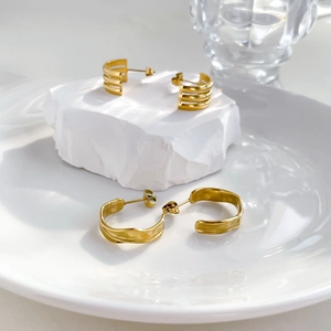 Chic three-layer gold hoop earrings and wavy studs on white mineral display stand