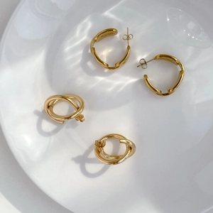 Elegante goldene Cross-Chain Creolen und C-förmige Stecker auf Wasserwellen-Hintergrund