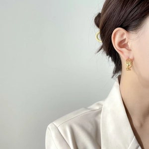 Detail von goldenen Kettenglied-Ohrringen an einem Modell in einem beigen Blazer