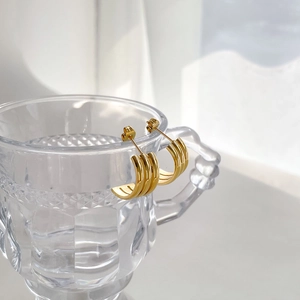 Close-up of triple-layered golden C-shaped hoop earrings on a textured glass rim