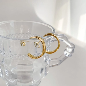 Macro detail of gold triple-layered C-shape hoop earrings on a textured glass rim