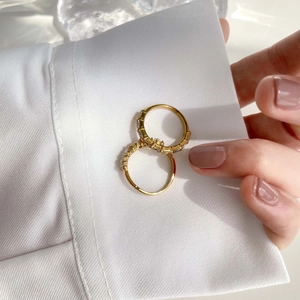 Detail view of two minimalist gold-plated rings with zircon stones on white fabric