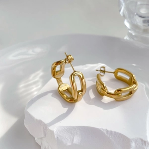 Detail von goldenen Kettenglied-Ohrringen auf weißem Steinblock für einen minimalistischen Look
