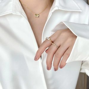 Detail of luxury gold zircon necklace and stacked rings worn with a white shirt