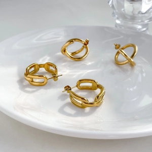 Elegante goldene Kettenglieder-Ohrringe und verschlungene Ringe auf Keramikteller