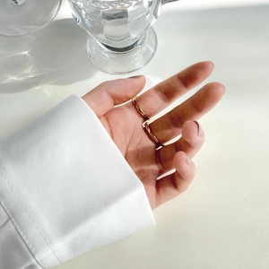 Minimalist gold double-ring worn on fingers with a sleek metallic finish and soft lighting