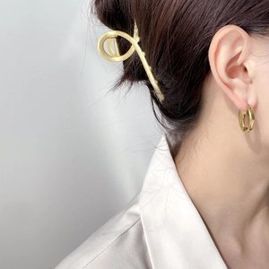 Détail d'une pince à cheveux dorée mate et de boucles d'oreilles ovales sur un modèle