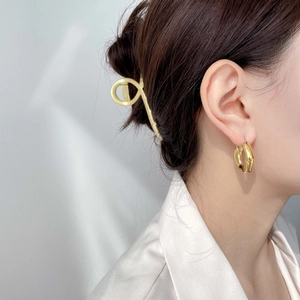 Détail d'une pince à cheveux dorée et de boucles d'oreilles texturées sur un modèle