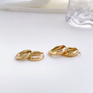 Gros plan de boucles d'oreilles créoles dorées en V sur un fond luxueux en soie blanche