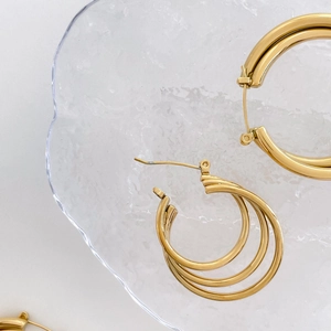 Macro shot of triple-layer golden hoop earrings on a transparent wave acrylic display
