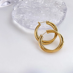 Macro detail of triple layered golden hoop earrings displayed on decorative glass