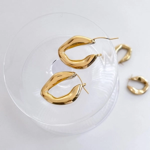 Gros plan de boucles d'oreilles losanges dorées polies sur un socle en verre