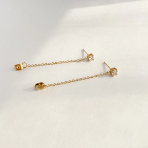 Detail view of golden chain stud earrings with white zircon and butterfly backs