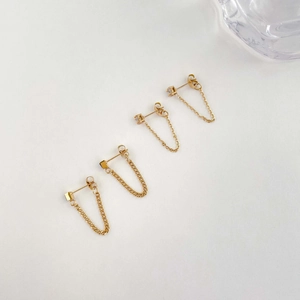 Detail of gold chain earrings with black zircon and minimalist cube studs set on light grey