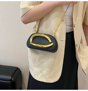 Detail of a black matte mini bag with striking gold metal ring buckle and chain strap