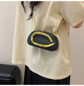 Black pill-shaped evening bag with a large gold metal emblem and delicate chain strap