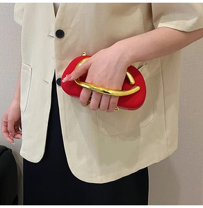 Detail of red velvet evening clutch with a bold gold metal handle held by a model