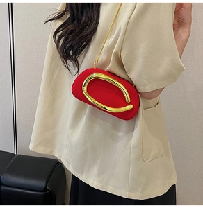 Detail of red crossbody evening bag featuring a gold circular handle and chain strap