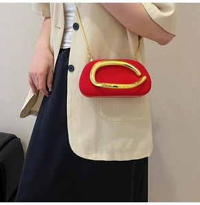 Detail of red crossbody bag with gold C-shaped metal buckle and chain on a model