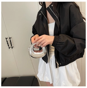 Detail of silver mirror acrylic mini handbag with metallic chain strap and black jacket