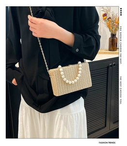 Detail of straw woven box bag featuring faux pearl handle and gold chain strap