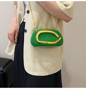 Detail of green mini clutch bag with golden chain and metallic accent on beige blazer