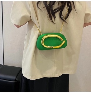 Close-up of green leather cylinder crossbody bag with golden C-buckle and chain strap