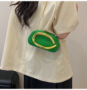 Detail of emerald green crossbody bag with gold oval ring and chain strap on model