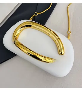 Macro detail of polished gold-plated metal chain and D-shaped pendant on white pebbles