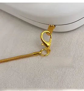 Close-up of detachable golden lobster clasp and sleek snake chain on a white box bag
