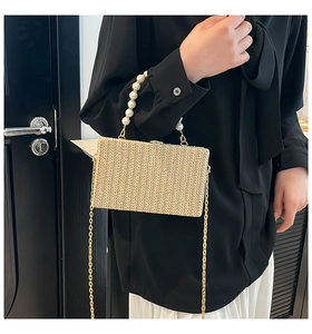 Detail of straw box bag with pearl handle and golden chain strap on a model