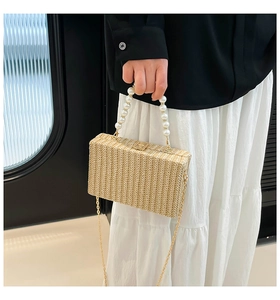 Detail of hand-woven straw box bag with large faux pearl handle and metal chain strap