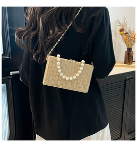 Detail of hand-woven straw box bag with large pearl handle and gold chain strap