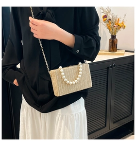Detail of a rectangular straw box bag featuring a pearl bead handle and gold chain strap