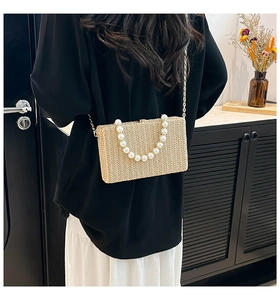 Detail of woven straw box bag with pearl bead handle and gold chain strap shown on model