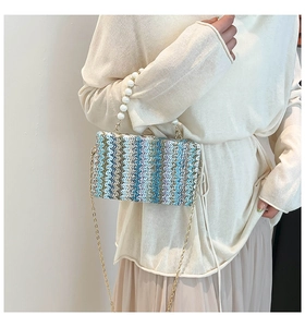Close-up of hand-woven straw bag with colorful patterns, pearl handle and gold chain