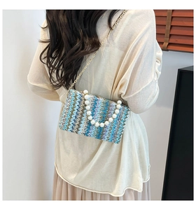 Close-up of woven straw bag with wavy pattern, faux pearl handle and metal chain strap