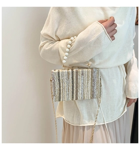 Detail of woven straw handbag featuring pearl beaded handle and gold chain strap