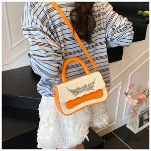 Detail of color-block crossbody bag with gothic silver emblem and orange strap shown on model