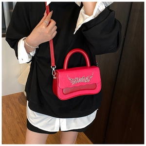 Detail of red small handbag with silver metal letter decor and round handle on a model
