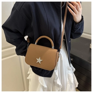 Detail of a brown woven handbag with a silver star ornament worn by a fashion model