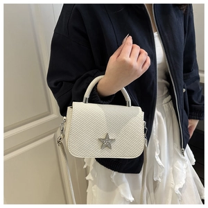 Detail einer cremeweißen gewebten Handtasche mit silbernem Stern und Lederstruktur