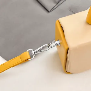 Macro detail of polished alloy hook and yellow leather strap on the color-block box bag