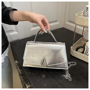 Detail of silver crocodile pattern handbag featuring metallic clasp and chain strap