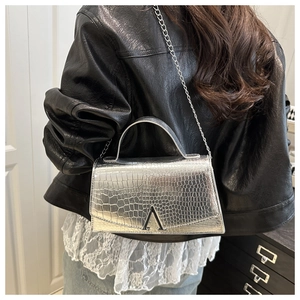 Close-up of silver crocodile embossed handbag with metal logo and chain strap details