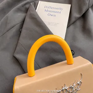 Close-up of beige handbag with yellow handle and stylish liquid metal ornament