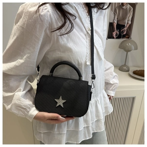Elegant black crossbody bag with rhinestone star worn by model in a stylish home setting