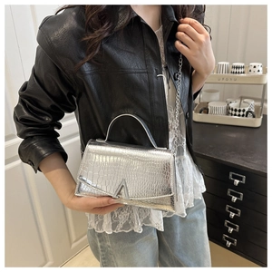 Detail of silver crocodile embossed handbag with V-shaped metal buckle and chain strap