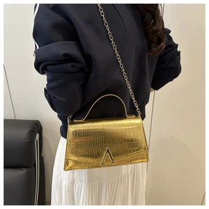 Detail of gold faux crocodile leather handbag featuring V-shaped buckle and chain strap
